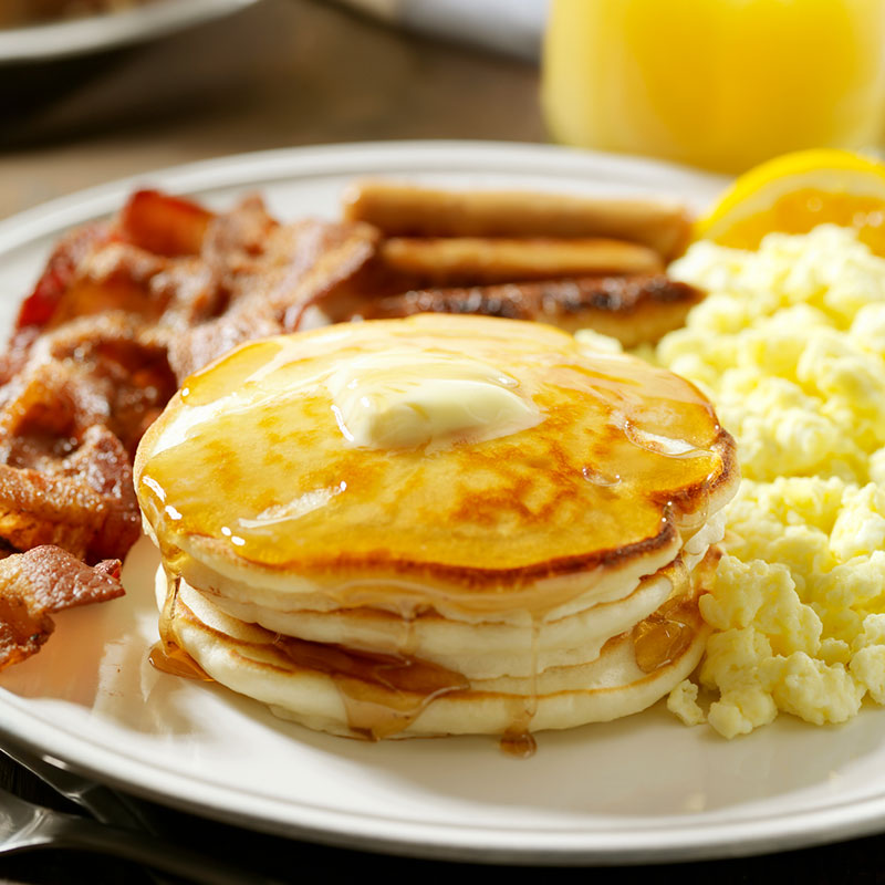Breakfast plate of pancakes, bacon, sausage and scrambled eggs.