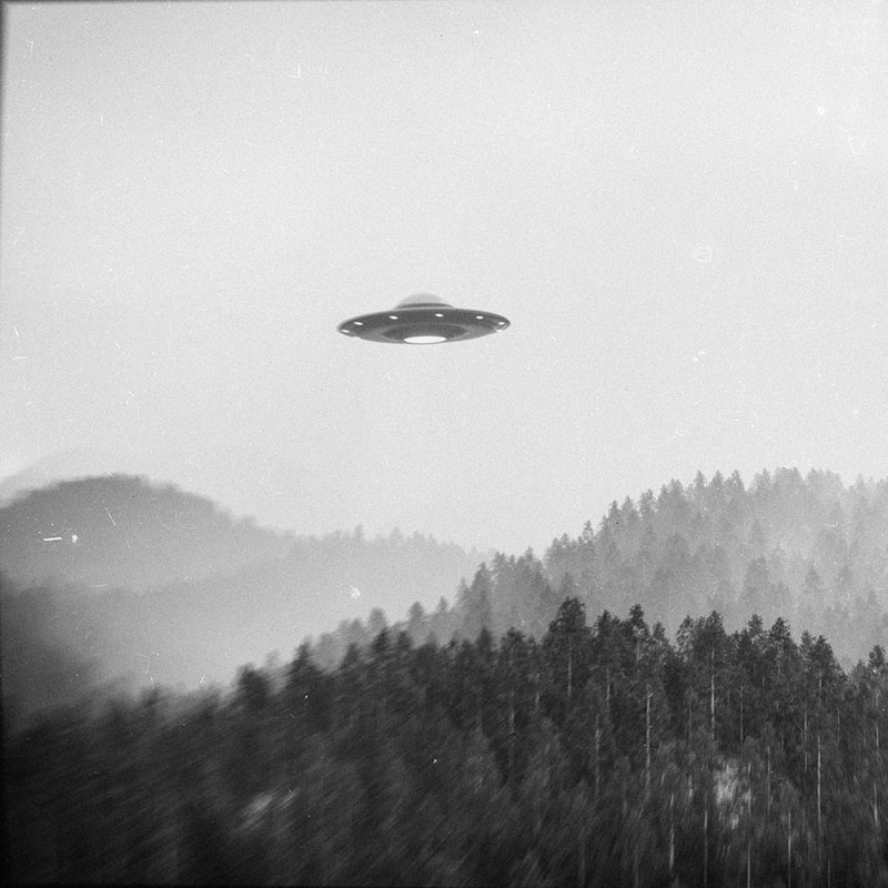 Black and white rendering of a UFO above a group of forested hills.