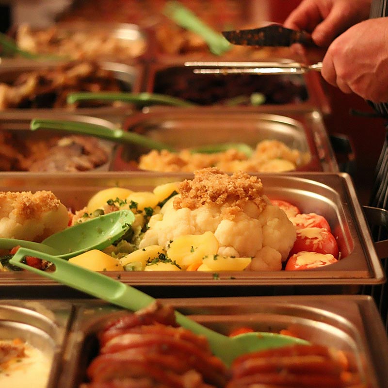 A chef serves a variety of entrees from a buffet table. Foods are set in metal trays with green ladles. Photo by guvo59 via pixabay.com