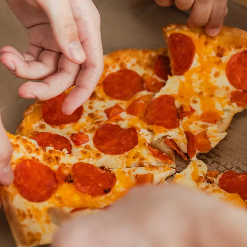 People reaching into a pizza box for slices of pepperoni pizza. Photo credit: Magnific by zavalishina.